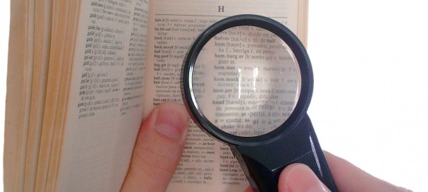 Hands holding a magnifying glass over a page of a dictionary